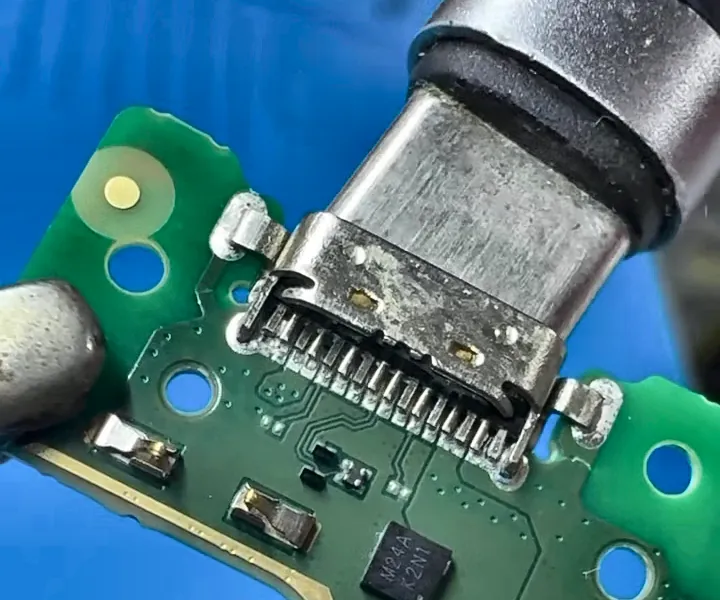 Placa de celular na bancada da Multi, com o conector de carga queimado sendo reparado